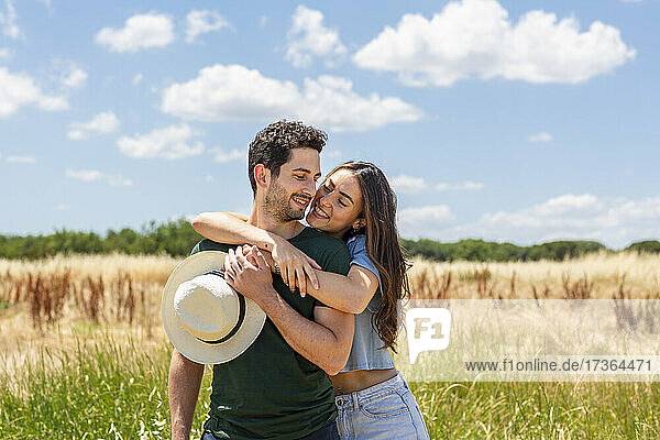 Smiling girlfriend embracing boyfriend at meadow on sunny day