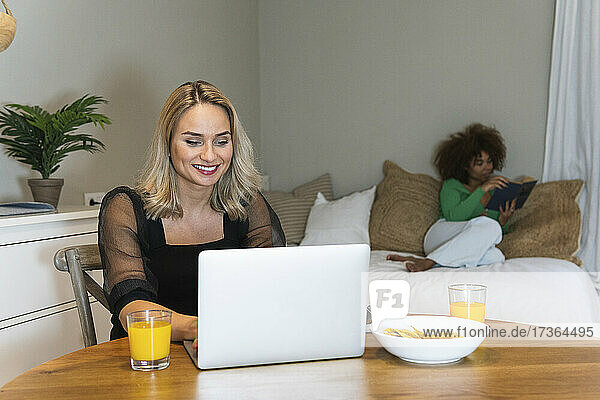 Junge Frau arbeitet zu Hause mit einem Freund an einem Laptop