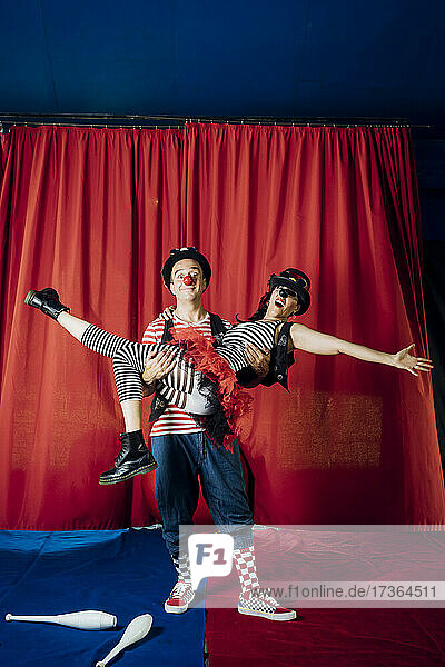 Männlicher Clown  der eine weibliche Darstellerin trägt  während er auf der Zirkusbühne auftritt