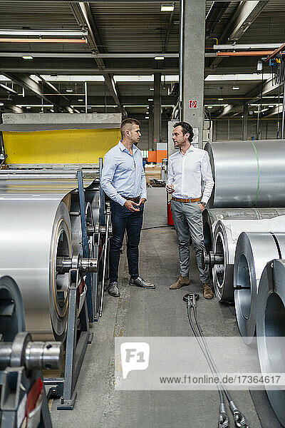 Businessmen having discussion while standing amidst steel rolls at industry