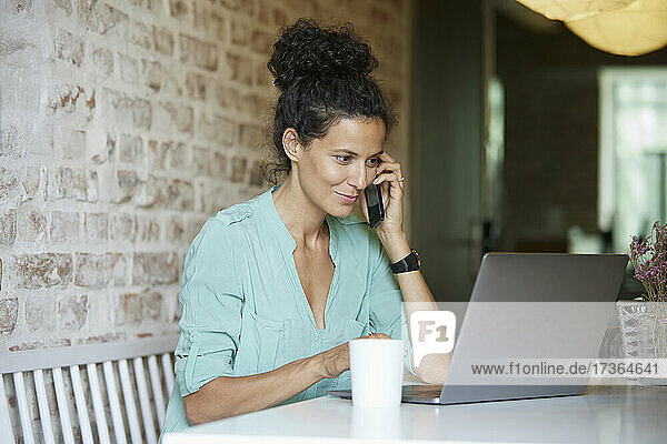 Weibliche Berufstätige  die am Arbeitsplatz mit dem Handy telefonieren und einen Laptop benutzen