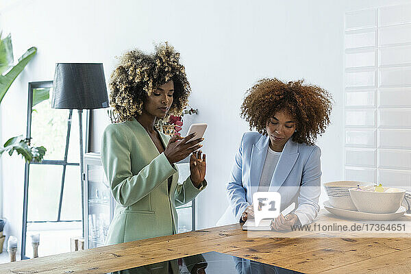 Junge Geschäftsfrau  die ein Smartphone benutzt  während eine Kollegin den Terminkalender auf dem Tisch betrachtet