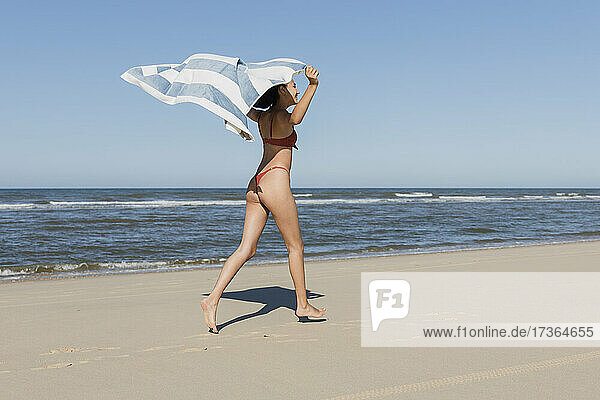 Frau winkt mit Handtuch beim Laufen am Strand im Urlaub