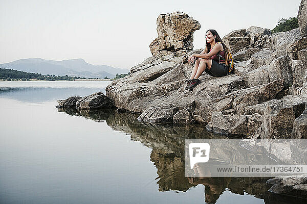 Lächelnde Wanderin schaut weg  während sie auf einem Felsen am See sitzt