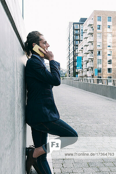 Businessman talking on mobile phone while leaning on wall