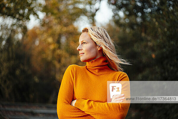 Woman looking away while standing with arms crossed during sunset