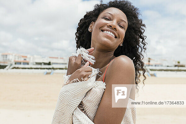 Smiling woman with eyes closed wearing beach towel on sunny day