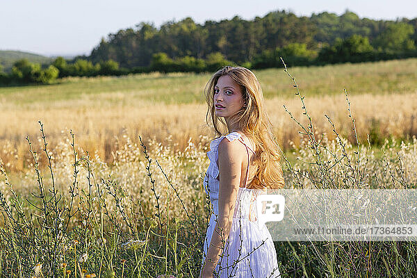 Schöne Frau in weißem Kleid steht inmitten von Pflanzen im Feld