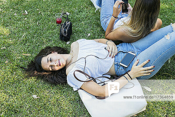 Junge Frau hört Musik und entspannt sich mit ihrer Freundin im Park