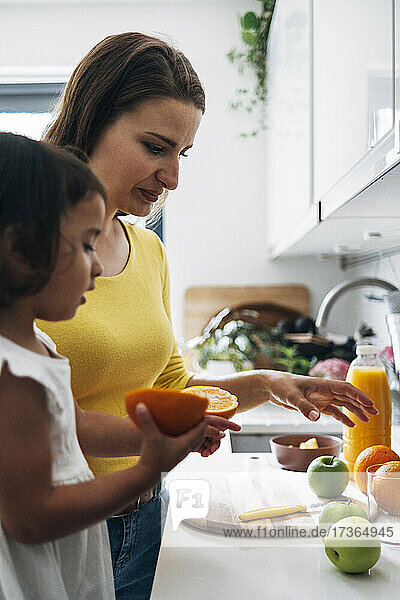 Daughter pointing at fruit while standing by mother in kitchen
