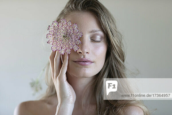 Junge schöne Frau mit Wildblume vor dem Auge im Studio