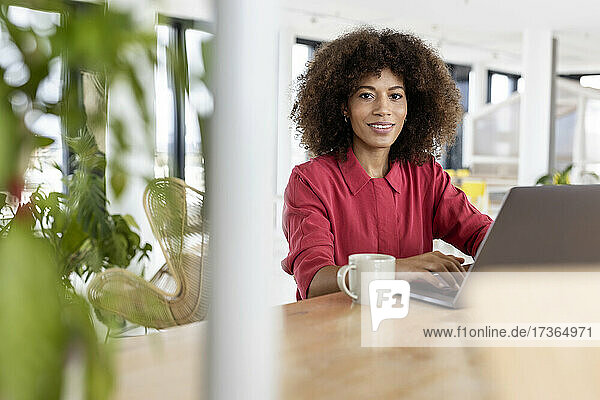 Afro-Geschäftsfrau mit Laptop lächelnd im Büro