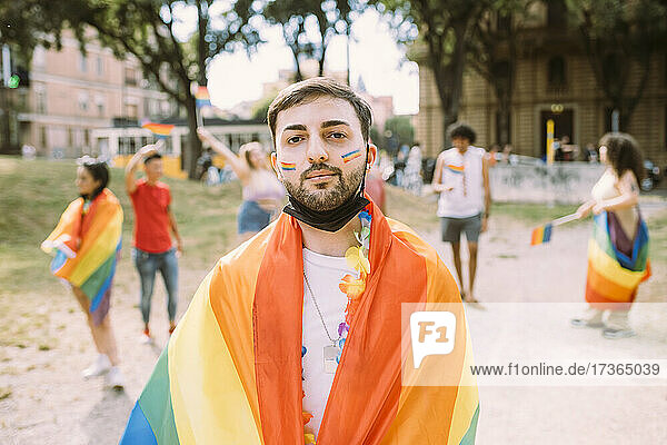 Junger Mann in Regenbogenfahne gehüllt auf der Pride-Veranstaltung während der COVID-19