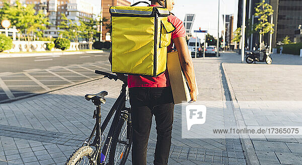 Delivery man carrying package while walking with bicycle on road