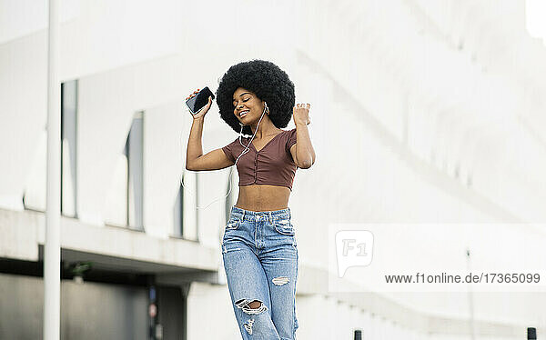 Afro woman with eyes closed listening music while dancing in city