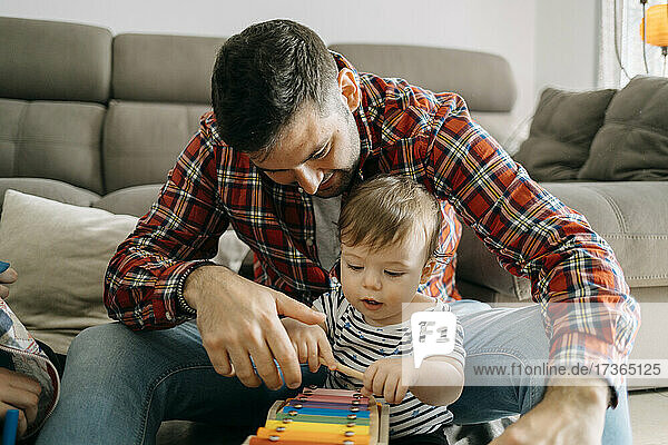 Father teaching xylophone to son in living room