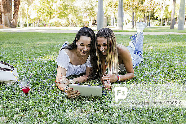 Young female friends sharing digital tablet while lying on grass at park