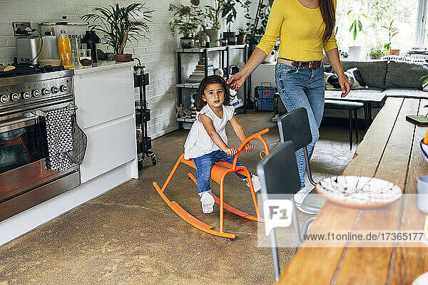 Mother standing by daughter playing on rocking horse at home