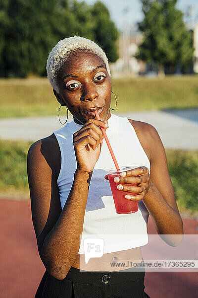 Woman drinking juice while standing at park