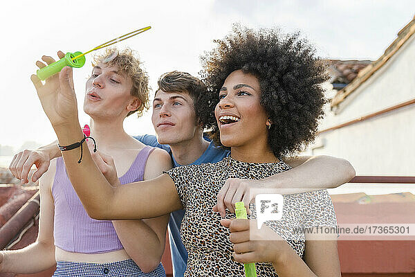 Junge multiethnische Freunde spielen mit Seifenblasen auf der Terrasse während einer Party