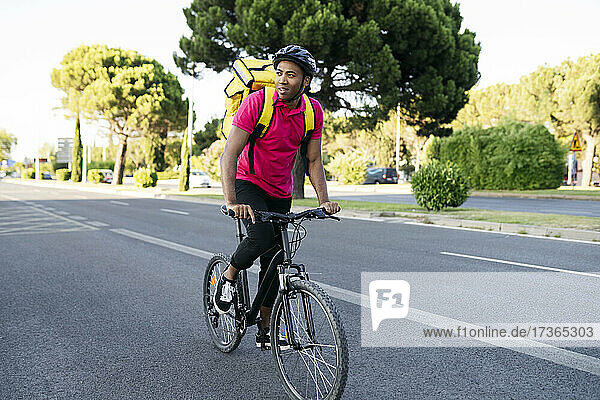 Delivery man looking away while riding bicycle on road