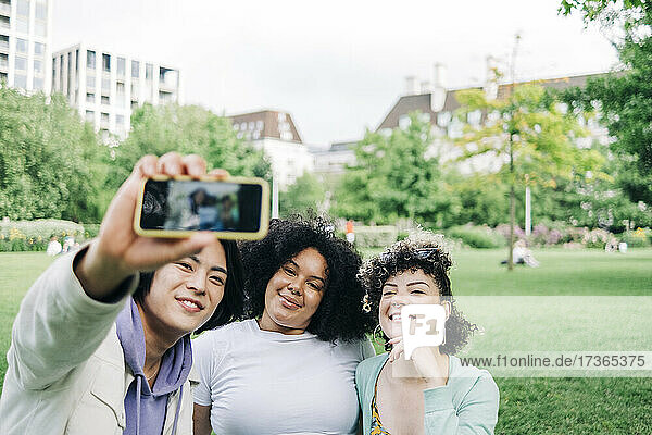 Smiling male and female friends taking selfie at park