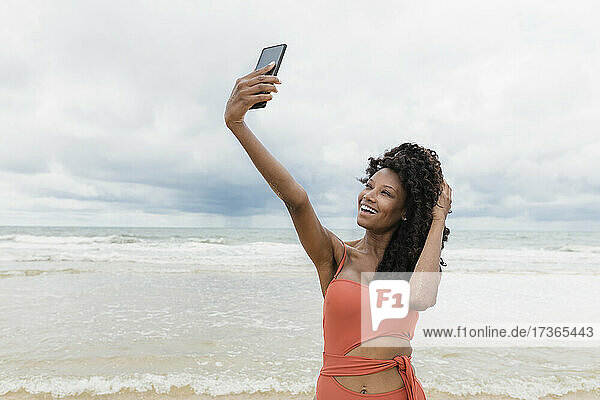 Happy beautiful woman taking selfie through mobile phone at beach