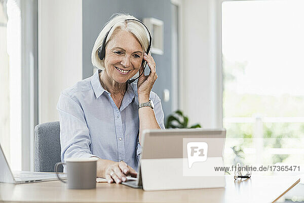 Verkäuferin stellt Headset ein  während sie im Büro zu Hause an einem digitalen Tablet arbeitet