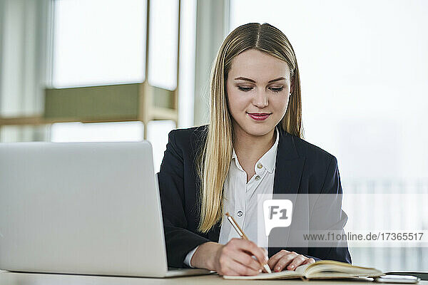 Teenager-Praktikant schreibt in Tagebuch  während er am Schreibtisch im Büro sitzt