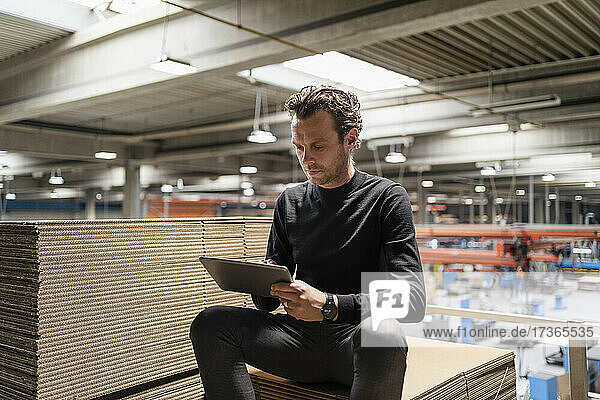 Businessman using digital tablet while sitting on cardboard stack