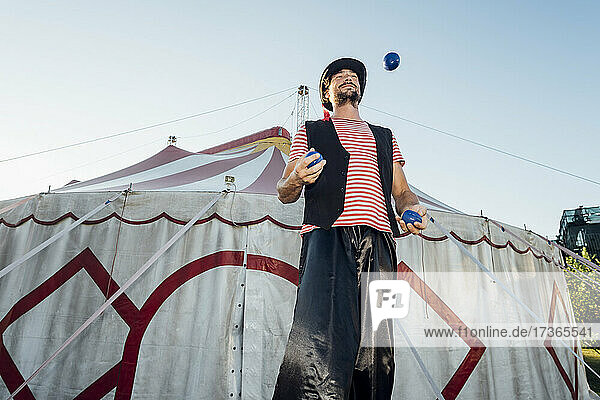 Männlicher Artist jongliert Bälle  während er vor einem Zirkuszelt steht