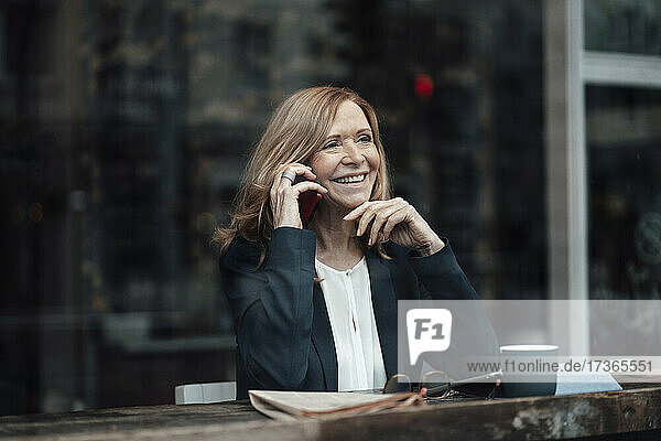 Glückliche ältere Geschäftsfrau mit blondem Haar  die in einem Café sitzt und mit ihrem Smartphone spricht