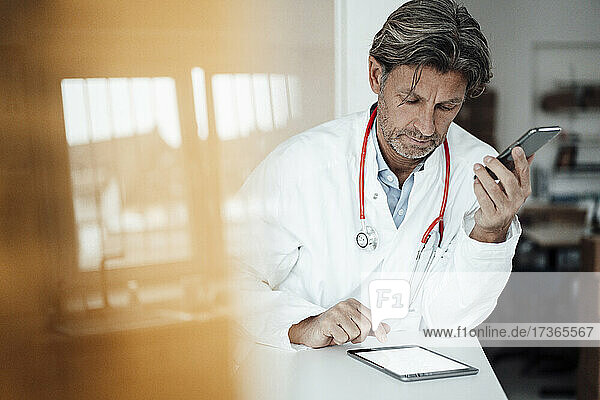Male healthcare worker using digital tablet while leaning on desk in clinic