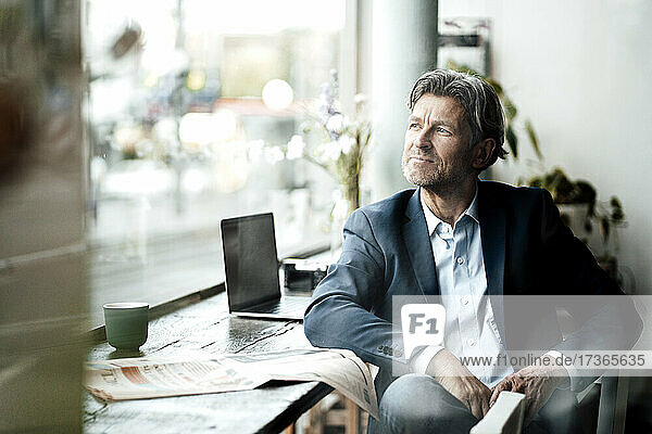 Männlicher Berufstätiger mit Zeitung sitzt am Tisch im Café und schaut durch das Fenster