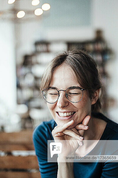 Fröhliche junge Frau mit Hand am Kinn in einem Cafe