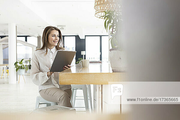 Weibliche Fachkraft mit digitalem Tablet auf einem Tisch im Büro sitzend