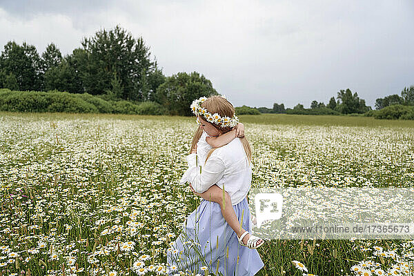 Mother carrying daughter while walking in chamomile field