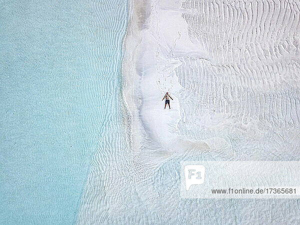 Luftaufnahme eines einsamen Mannes beim Sonnenbaden am Sandstrand der Insel Thulusdhoo