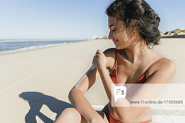 Frau  die an einem sonnigen Tag am Strand Sonnenschutzmittel aufträgt
