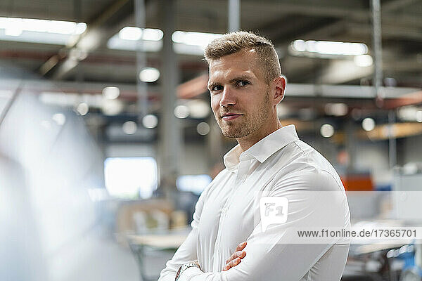 Confident young male professional with arms crossed at factory