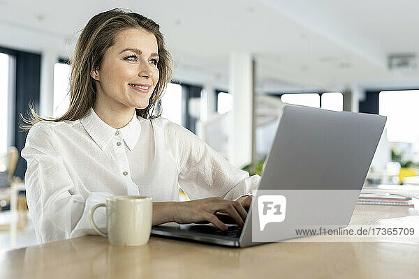Lächelnde Geschäftsfrau mit Laptop auf dem Tisch im Büro