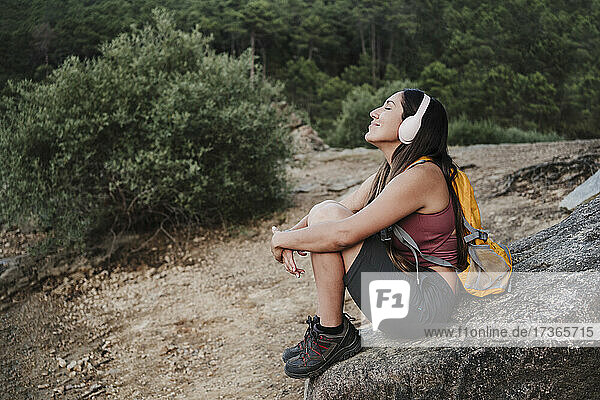 Weiblicher Rucksacktourist mit geschlossenen Augen  der auf einem Felsen sitzend Musik hört