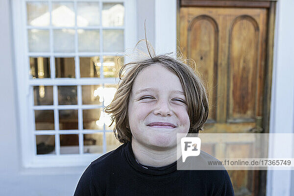 Porträt eines Jungen  der lächelnd vor seinem Haus posiert