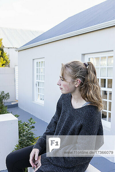 Teenager-Mädchen sitzt vor einem Haus auf einer niedrigen Mauer und wartet