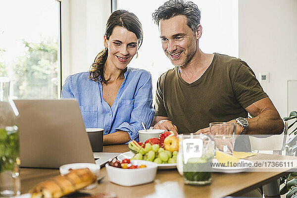 Mann und Frau beobachten Laptop beim Frühstück zu Hause