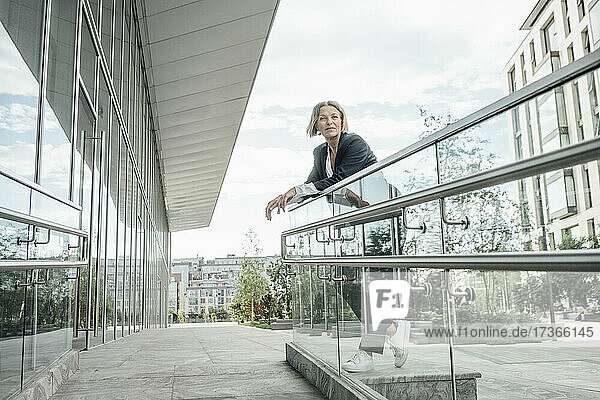 Nachdenkliche Geschäftsfrau  die sich auf ein Geländer im Büropark stützt