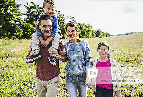 Lächelnde Familie beim Spaziergang auf einer Wiese an einem sonnigen Tag
