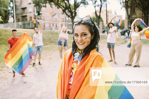 Lächelnde Frau in Regenbogenfahne eingewickelt im Park
