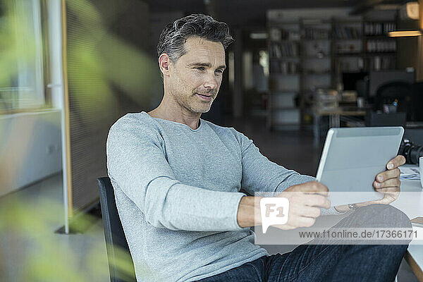 Männlicher Geschäftsmann  der ein digitales Tablet bei der Arbeit im Büro benutzt