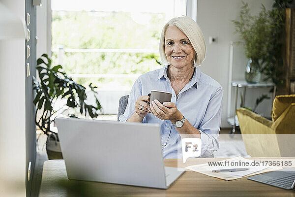 Geschäftsfrau hält Kaffeetasse am Schreibtisch im Heimbüro